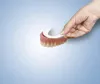 A hand is holding a denture liner over a set of dentures. Produktbild-Vorschau
