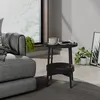 A black side table with a cup of coffee and a magazine on it, next to a gray sofa in a living room. Náhled obrázku produktu