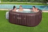 Four people relaxing in a brown inflatable hot tub on a grassy lawn next to a swimming pool. Produktbild-Vorschau
