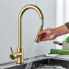 A hand is holding a pull-down faucet head, with water spraying into a sink. There are some vegetables on a cutting board in the background. Produktbild-Vorschau