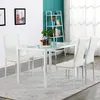 A dining set with a glass-top table and four white chairs in a room with a teal accent wall and a white ladder shelf. Podgląd zdjęcia produktu