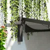 A close-up view of a black metal pergola structure with hanging green plants and some pink and orange flowers in a pot. Náhľad obrázku produktu