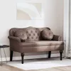 A brown Chesterfield sofa is shown in a room with a painting on the wall and a small black table to the left. Náhľad obrázku produktu