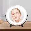 A woman's face is reflected in a lighted makeup mirror.