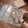 A person is shown putting clothes into a vacuum seal bag on a wooden floor. Podgląd zdjęcia produktu