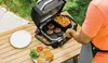 A person is grilling burgers and fries outdoors on a wooden table. Anteprima dell’immagine prodotto
