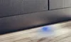 A close-up shot of the bottom of a dark gray cabinet with a blue light glowing on the wooden floor beneath it. Produktbild-Vorschau