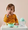 A baby sitting in a high chair eating food from a bowl, with a sippy cup next to it. Produktbild-Vorschau