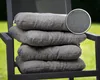 A stack of four grey seat cushions on a dark grey chair outdoors, with a close-up inset of the fabric texture. Produktbild-Vorschau