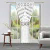 A decorative curtain panel hanging in a window with a small table and vase to the left and an armchair to the right. Náhľad obrázku produktu