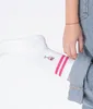 A person's leg wearing a white sock with pink stripes and a wine glass graphic, with jeans rolled up. Produktbild-Vorschau