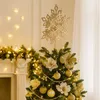 A decorated Christmas tree with a snowflake topper and golden ornaments, set against a backdrop of a fireplace with festive lights. Náhled obrázku produktu