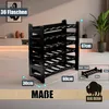 A black plastic wine rack is shown in a room setting with some decorative items and a plant in the background. Dimensions are indicated with text overlays. Produktbild-Vorschau