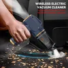 A hand is holding a blue and gold wireless electric vacuum cleaner, cleaning debris from a car floor. Produktbild-Vorschau