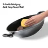 A hand is cleaning a wok pan with a yellow sponge. Produktbild-Vorschau