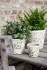 Three decorative plant pots with green floral patterns sit on a wooden table in front of a brick wall. Podgląd zdjęcia produktu