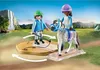 Two children playing with a horse and riding accessories in a natural outdoor setting with a waterfall in the background. Produktbild-Vorschau