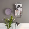 A wall-mounted magazine rack with magazines, a clock, and a vase of flowers in a room. Náhľad obrázku produktu