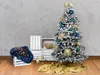 A decorated artificial Christmas tree with a snowy appearance, set against a textured wall and wooden floor, with decorative elements like crates, a furry throw with lights, and golden ornaments. Podgląd zdjęcia produktu