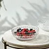 A clear glass bowl filled with mixed berries sits on a marble tabletop, with soft shadows cast on the wall behind it. Produktbild-Vorschau