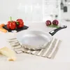 A frying pan is set on a striped cloth on a wooden table, with ingredients like bell peppers, carrots, onions, and cheese nearby. Produktbild-Vorschau