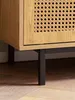 Close-up of the bottom corner of a wooden cabinet with a woven front panel, resting on black metal legs. Produktbild-Vorschau