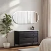 A modern bedroom or dressing area with a dresser and a large oval mirror above it, a potted plant to the left, and curtains in the background. Voir les images du produit