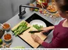 A person is preparing food in a kitchen, with a sink, faucet, cutting board, and various ingredients visible. Produktbild-Vorschau