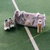 A duffel bag, a pair of sneakers, and a water bottle are placed on a green surface with a white line, resembling a sports field. Produktbild-Vorschau