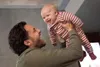 A father is holding his baby up in the air, both smiling. Produktbild-Vorschau