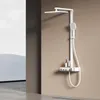 A modern white shower system mounted on a beige wall, with a glimpse of a minimalist outdoor scene in the background. Podgląd zdjęcia produktu