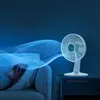 A white fan is blowing air, represented by blue digital particles, towards a person sleeping on a couch. Náhľad obrázku produktu