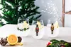 Three stemless wine glasses with festive Christmas designs, filled with ice and lemon slices, sit on a table next to a halved lemon and pinecones. A decorated Christmas tree is visible in the background. Produktbild-Vorschau