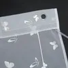 A close-up view of the top edge of a white sheer curtain with a butterfly pattern and grommets. Produktbild-Vorschau