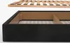 A close-up view of a black upholstered bed frame with a wooden slat base partially inserted. Produktbild-Vorschau