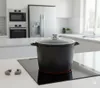 A black pot with a glass lid sits on a black induction stovetop in a modern kitchen. Produktbild-Vorschau