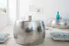 A living room scene with two hammered metal coffee tables, decorative pillows, and a window with natural light. Produktbild-Vorschau