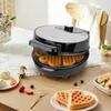 A waffle maker is shown on a table with waffles and other food items. Produktbild-Vorschau