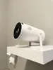 A white projector is mounted on a white shelf against a light gray wall. Produktbild-Vorschau