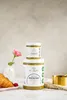 Two jars of pistachio paste are stacked on top of each other, with a croissant and raspberries in the foreground, and a pink rose in a vase to the left. Produktbild-Vorschau