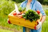 A person holding a wooden crate filled with fresh vegetables in a garden. Produktbild-Vorschau