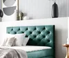 A close-up view of a green velvet box spring bed with white pillows and a gray blanket. Produktbild-Vorschau