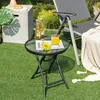 A small round glass-top bistro table with a black metal frame is set up on a green lawn next to a lounge chair and a concrete side table. Two bottles of beer and a glass of orange juice are on the table, along with a yellow flower and a magazine. Anteprima dell’immagine prodotto