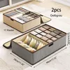 Two fabric storage boxes with dividers are shown on a carpeted floor. The boxes are filled with folded clothes, likely underwear or socks. Dimensions are indicated on the boxes. Produktbild-Vorschau
