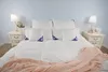 A neatly made bed with white bedding, pillows, and a pink throw blanket. Produktbild-Vorschau
