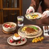 A table setting with various dishes, including a steak, dessert, and fruit salad, with a person serving the fruit salad. Náhled obrázku produktu