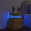 A wooden nightstand with blue LED lighting is placed next to a bed in a dimly lit bedroom. Podgląd zdjęcia produktu