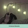 A string of star-shaped LED lights is draped over a white crib or bed frame, with a stuffed dog toy resting on a pillow in the foreground. Náhľad obrázku produktu