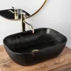 A black oval countertop sink with gold veining, a gold faucet, and a gold-rimmed mirror reflecting the faucet and sink. Produktbild-Vorschau