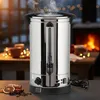A stainless steel hot water dispenser is shown in a cozy setting with a fireplace and decorative lights in the background. Náhled obrázku produktu
